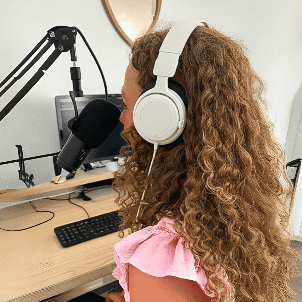 Blog and podcast danielle gray recording podcast wearing white head phones and talking into a mic